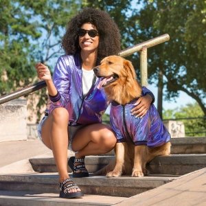 moça vestida com uma jaqueta bomber holográfica roxa passeando com seu cachorro que também esta usando uma jaqueta bomber holográfica roxa para cachorro
