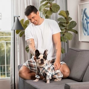 homem sentado do sofá usando pijama lulli camiseta branca e short xadrez azul com um cachorro usando o pijama pet lulli xadrez azul